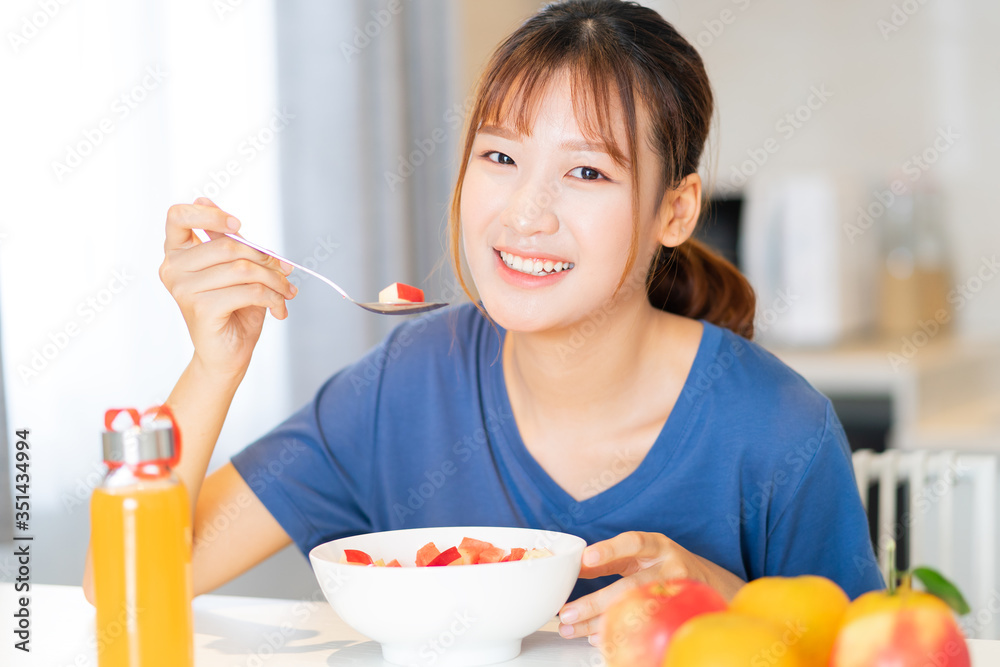 一位年轻的亚洲妇女在厨房里吃水果早餐