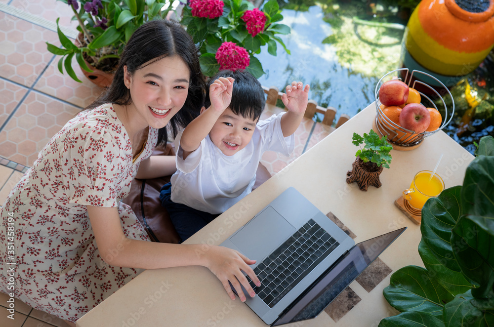 亚洲母亲在家里的花园里用笔记本电脑教儿子