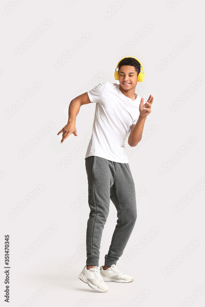 African-American teenager dancing and listening to music against light background