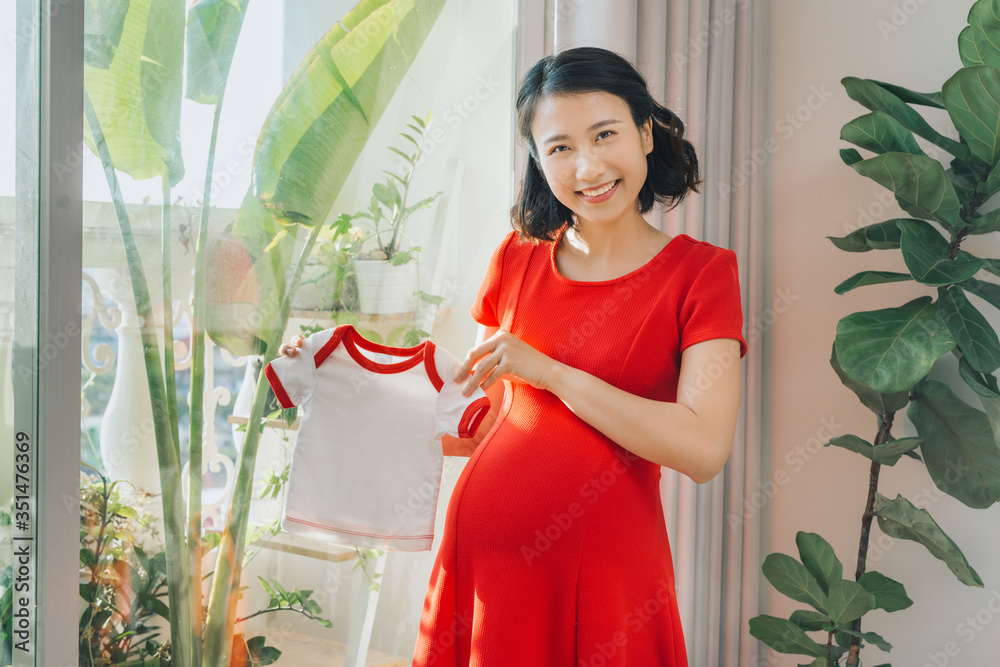 孕妇靠着窗户站着，手里拿着婴儿布。