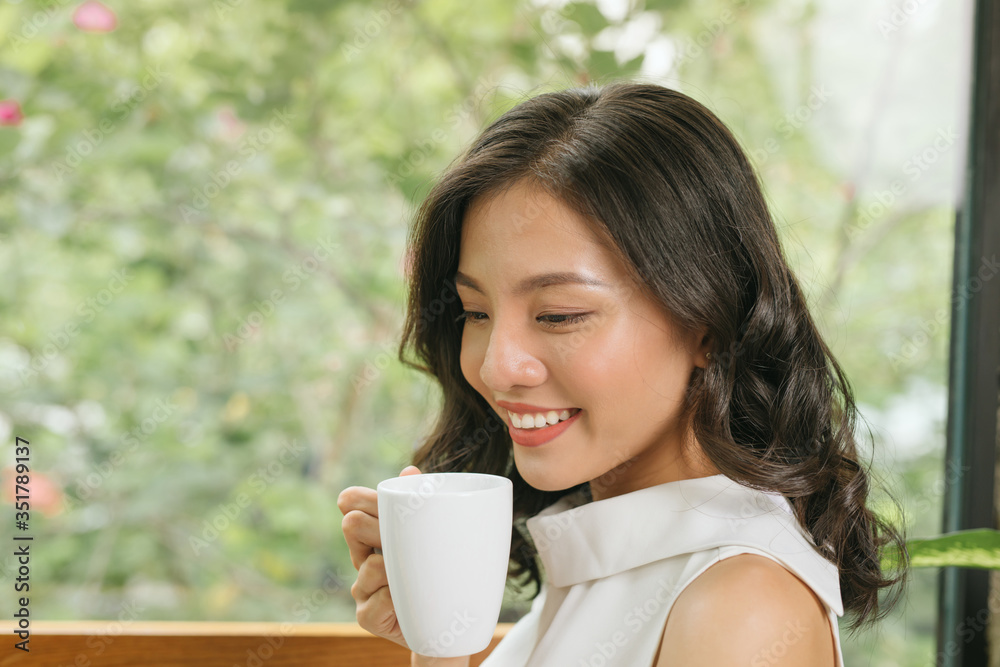 自由职业女性拿着咖啡杯，在咖啡馆的桌子上使用笔记本电脑