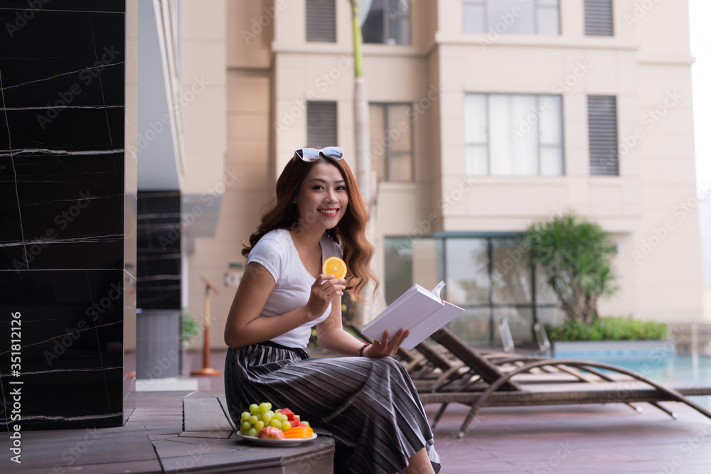 Woman reading a book near the water pool.