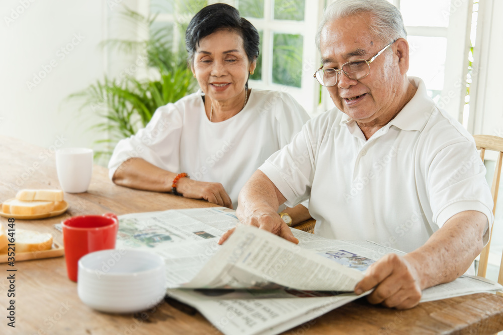 An Asian elderly couple reading a newspaper.