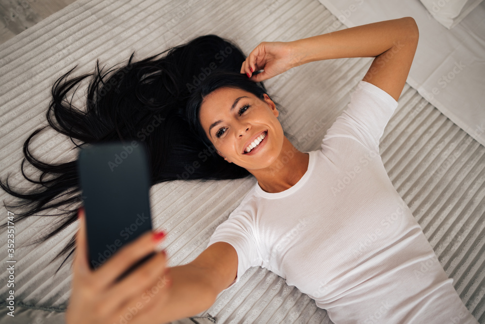 Beautiful relaxed woman taking selfie on bed.