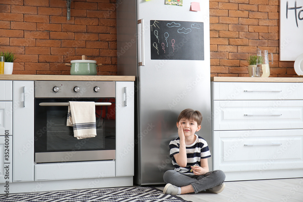 Little boy near chalkboard on refrigerator in kitchen