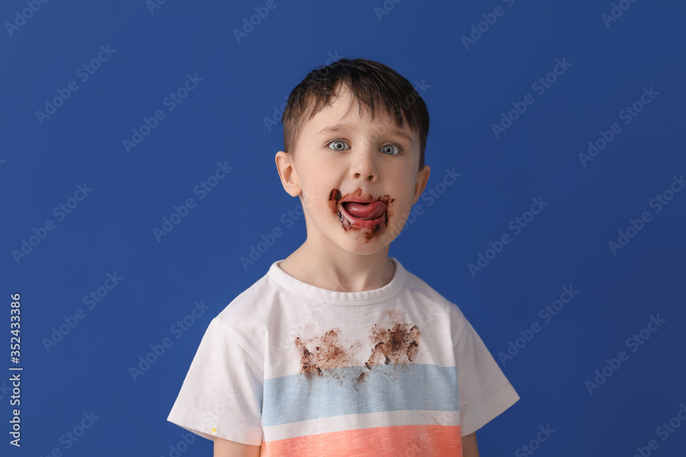 Little boy in dirty clothes eating of chocolate on color background