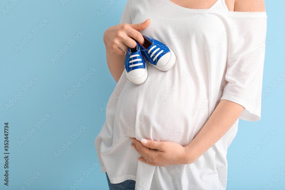 Beautiful pregnant woman with baby shoes on color background