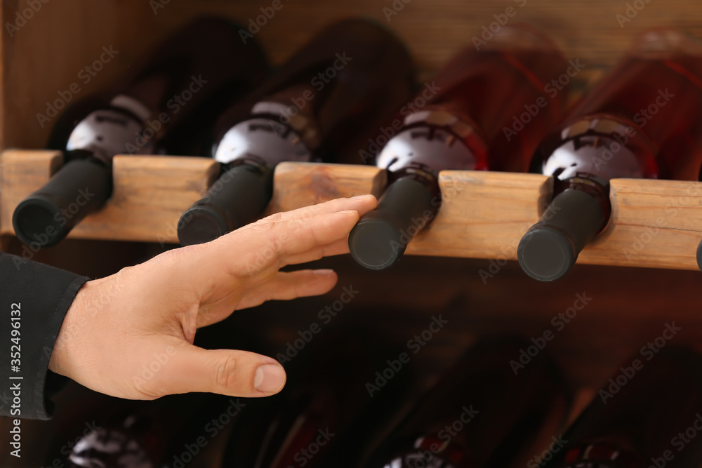 Man choosing bottle of wine in cellar, closeup