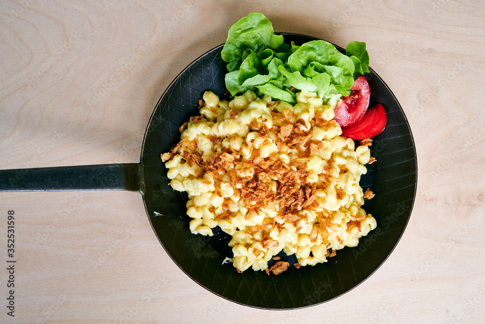 Bayrische Käsepätzle Kasspatzen mit Röstzwiebeln in einer Eisenpfanne auf einem Holztisch