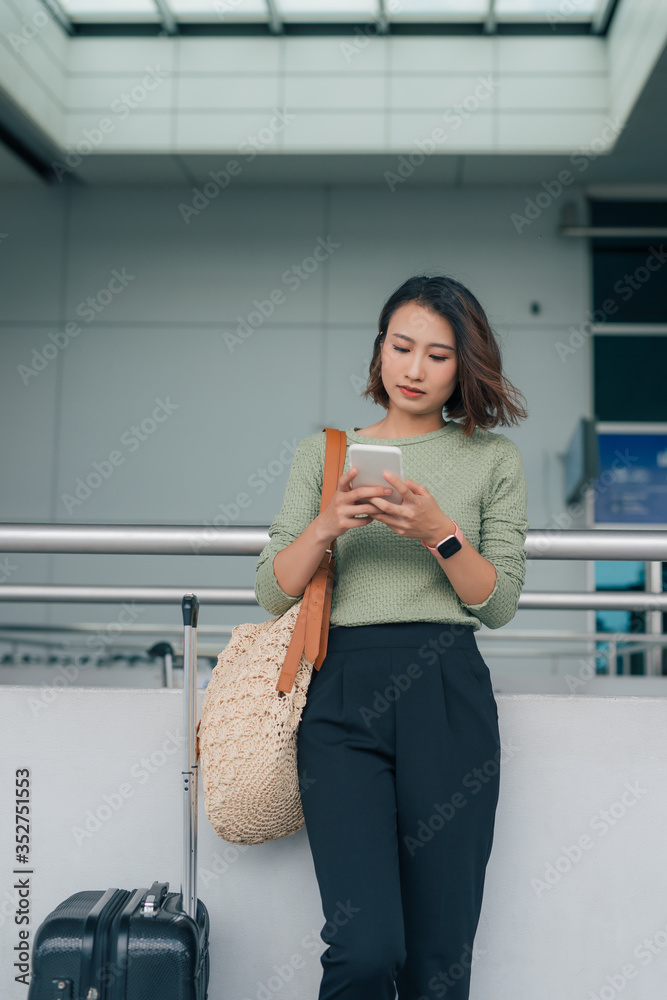 商务女性出差时拿着行李站在机场使用智能手机