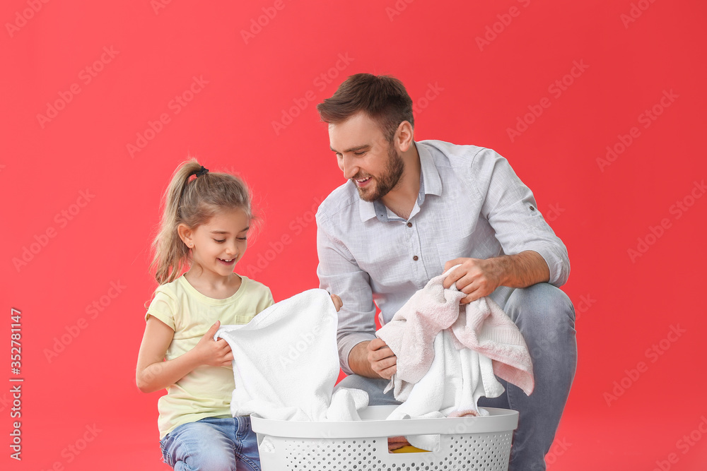 Father and little daughter with laundry on color background