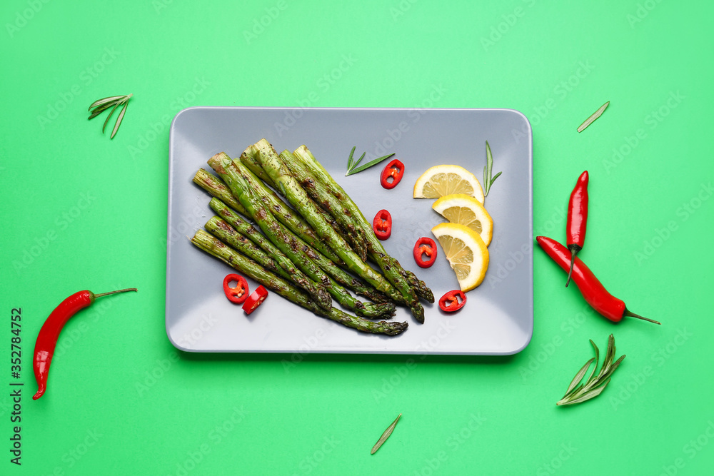 Cooked asparagus with chili pepper and lemon on color background