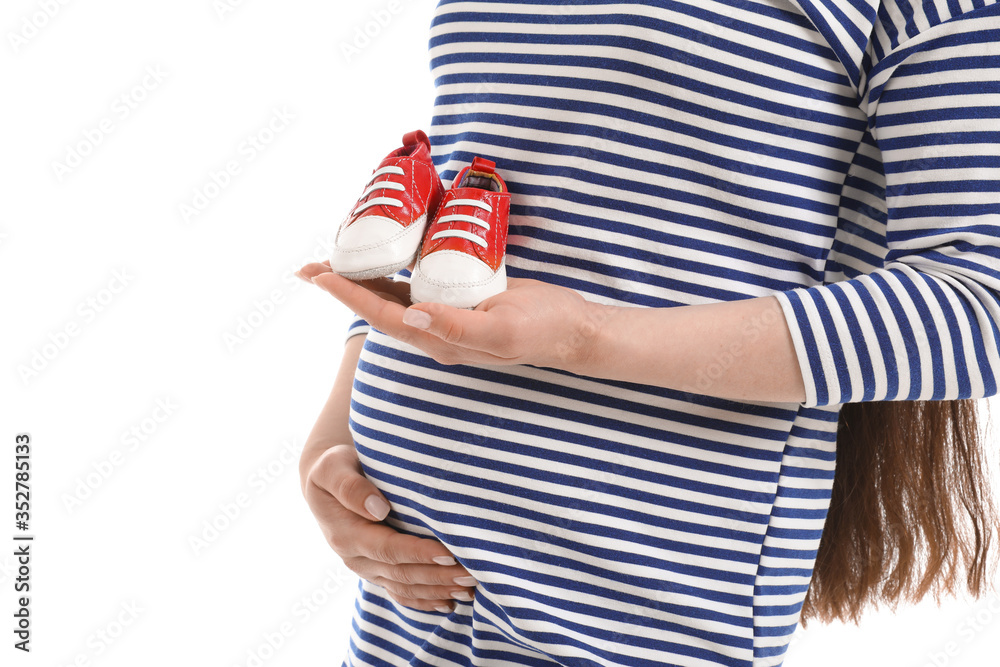 Beautiful pregnant woman with baby shoes on white background