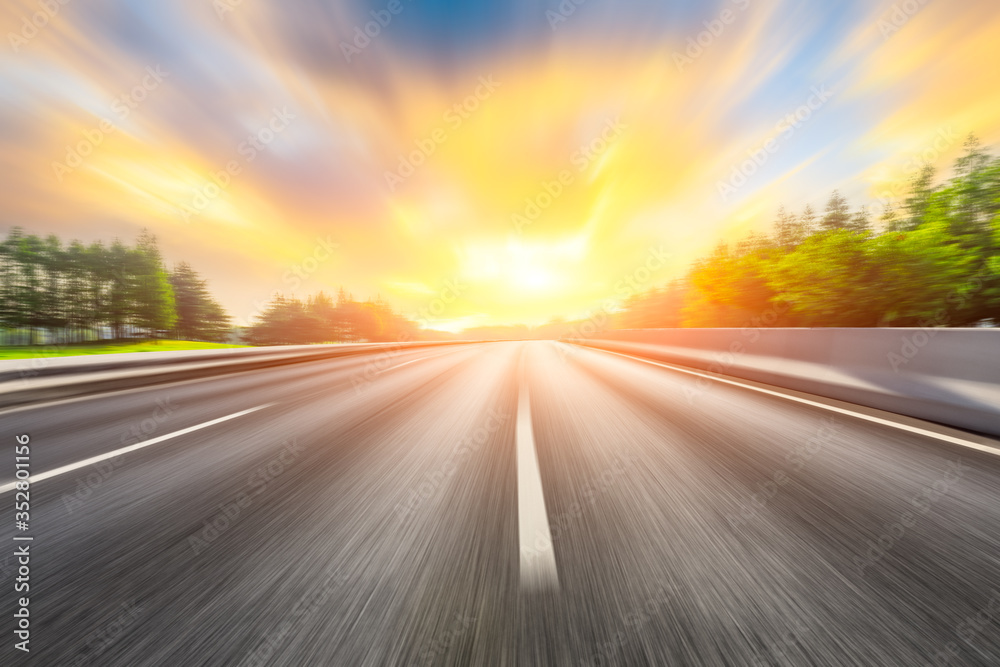 Fast moving asphalt highway and green forest at sunset.