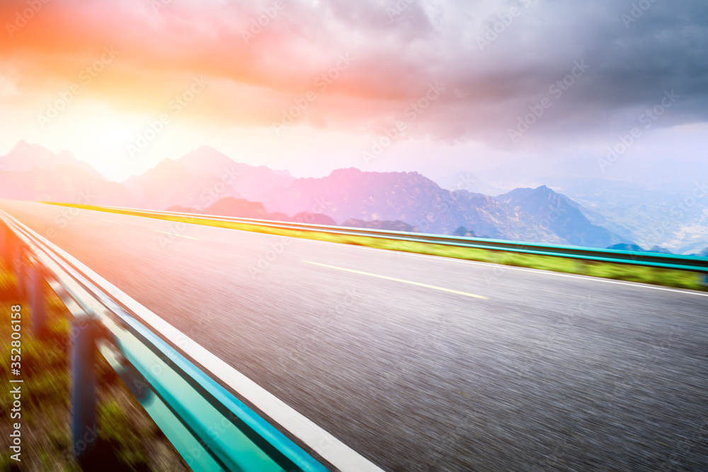 Motion blurred mountain road,asphalt roads and mountains with sky clouds at sunset.