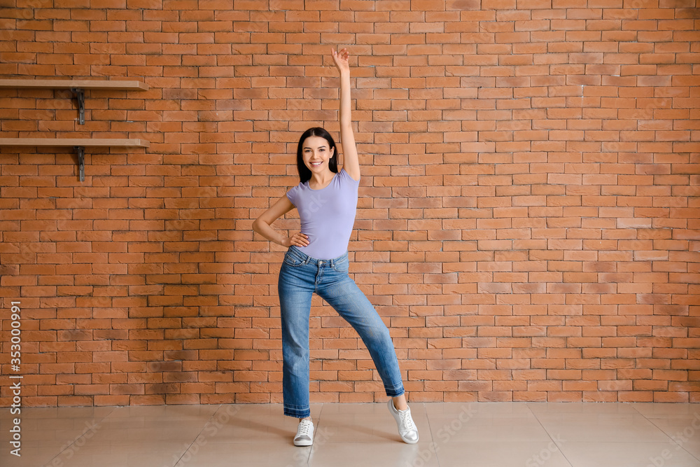 Beautiful young woman dancing near brick wall