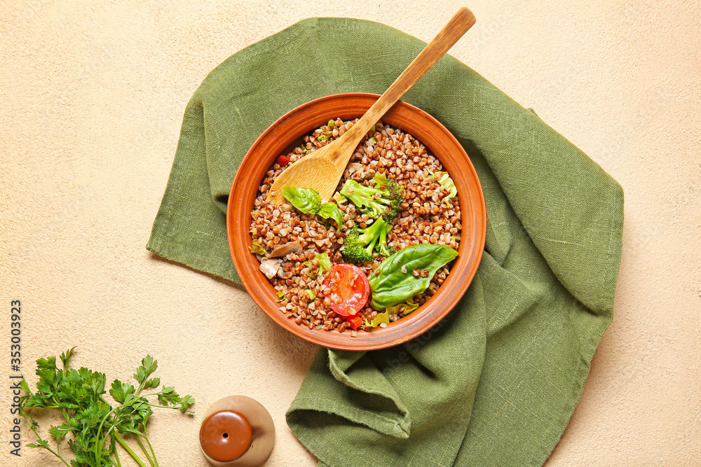 Bowl of tasty buckwheat porridge and vegetables on color background