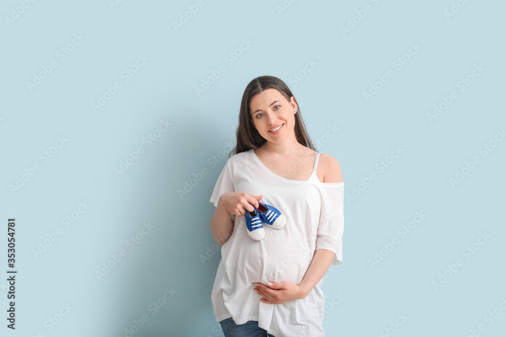 Beautiful pregnant woman with baby shoes on color background