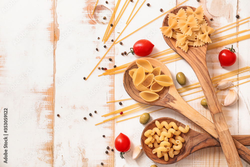 Different uncooked pasta with spices and vegetables on white wooden background