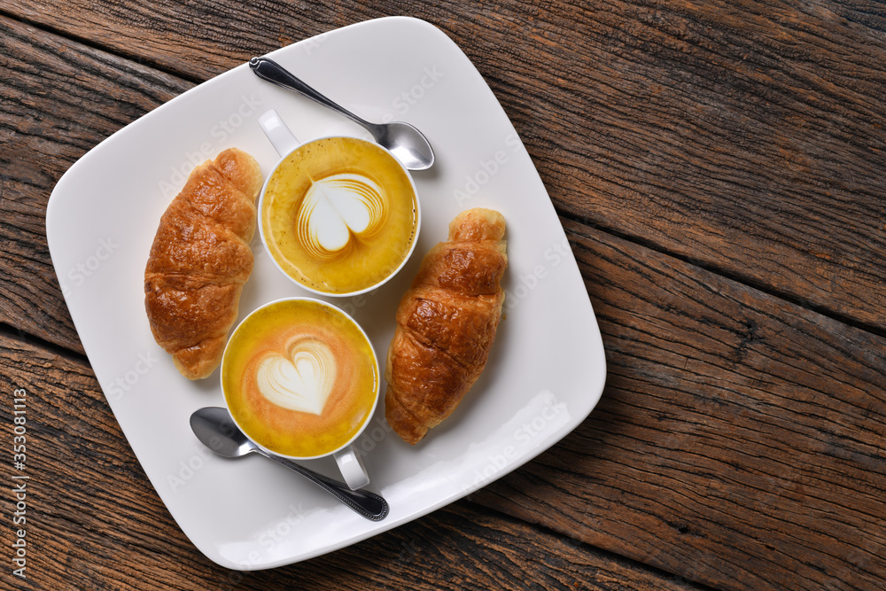 Top view cup of coffee latte and croissant on old wooden table.