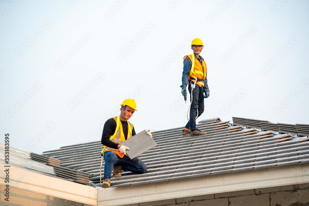 Roofer worker in special protective workwear and gloves installing new roof under construction resid