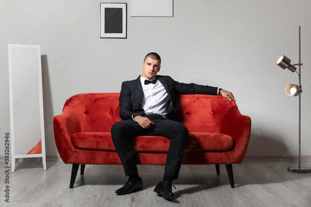 Handsome young man in elegant suit sitting on sofa indoors