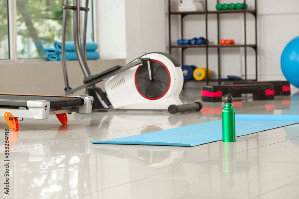 Yoga mat and bottle of water on floor in gym