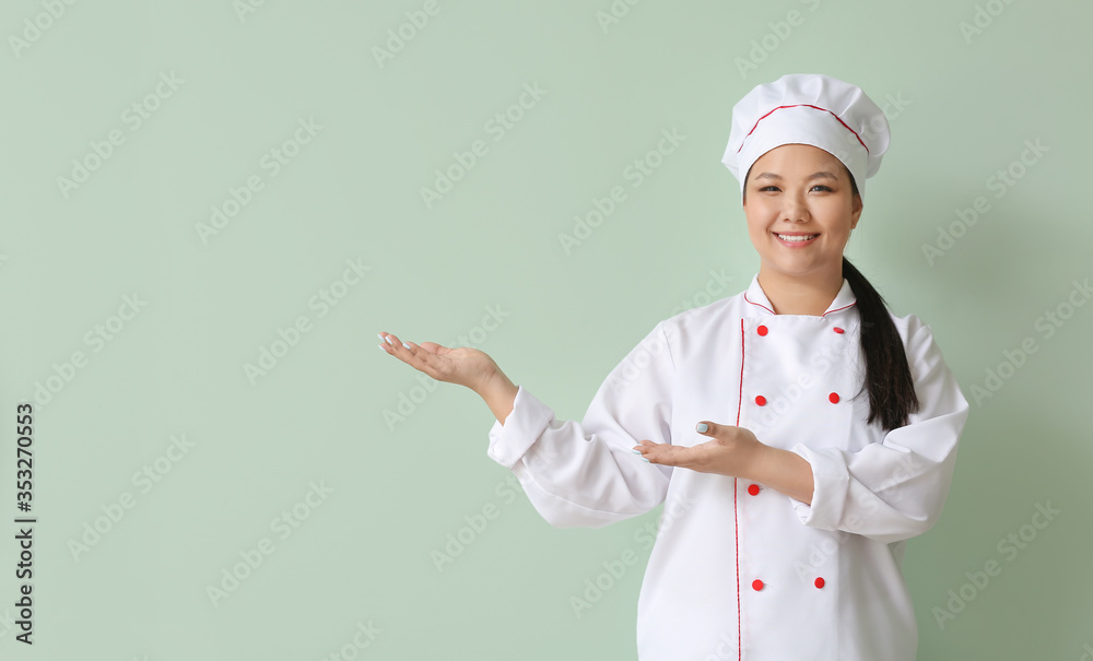 Beautiful Asian chef showing something on color background