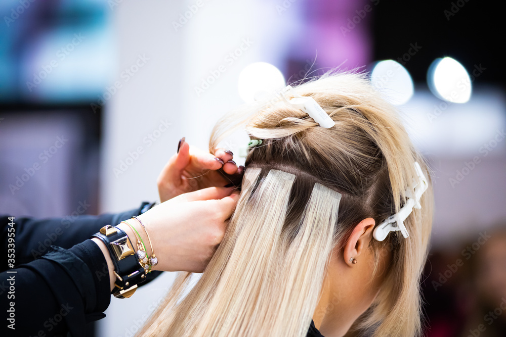 Professional hairdresser making hair extensions for blonde girl in a beauty salon