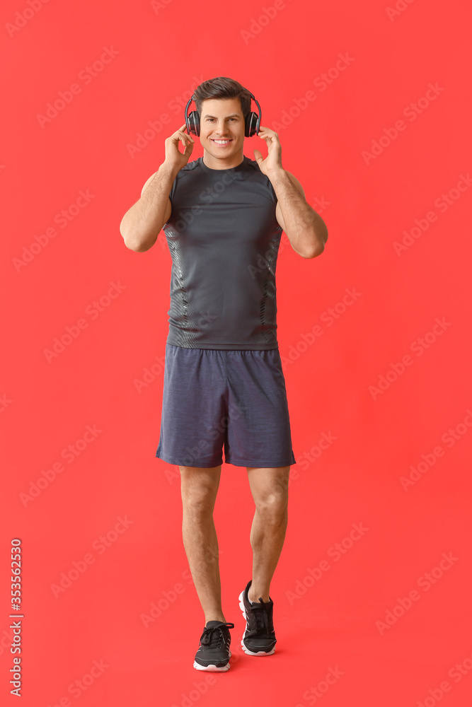 Sporty young man listening to music on color background