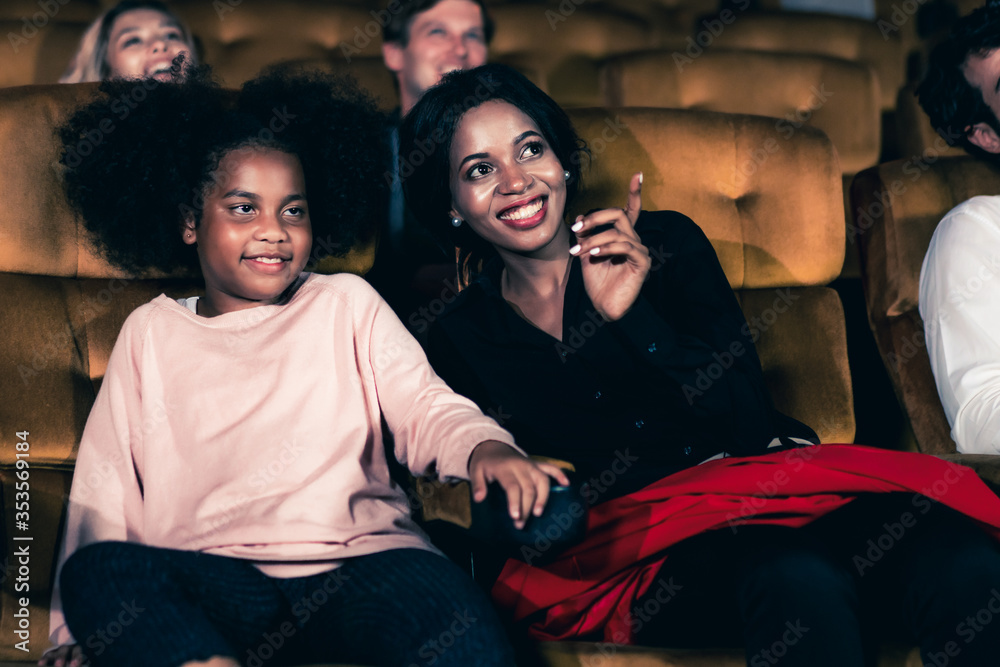 Woman enjoy to watch a movie with her daughter at the cinema smiling and laughing together