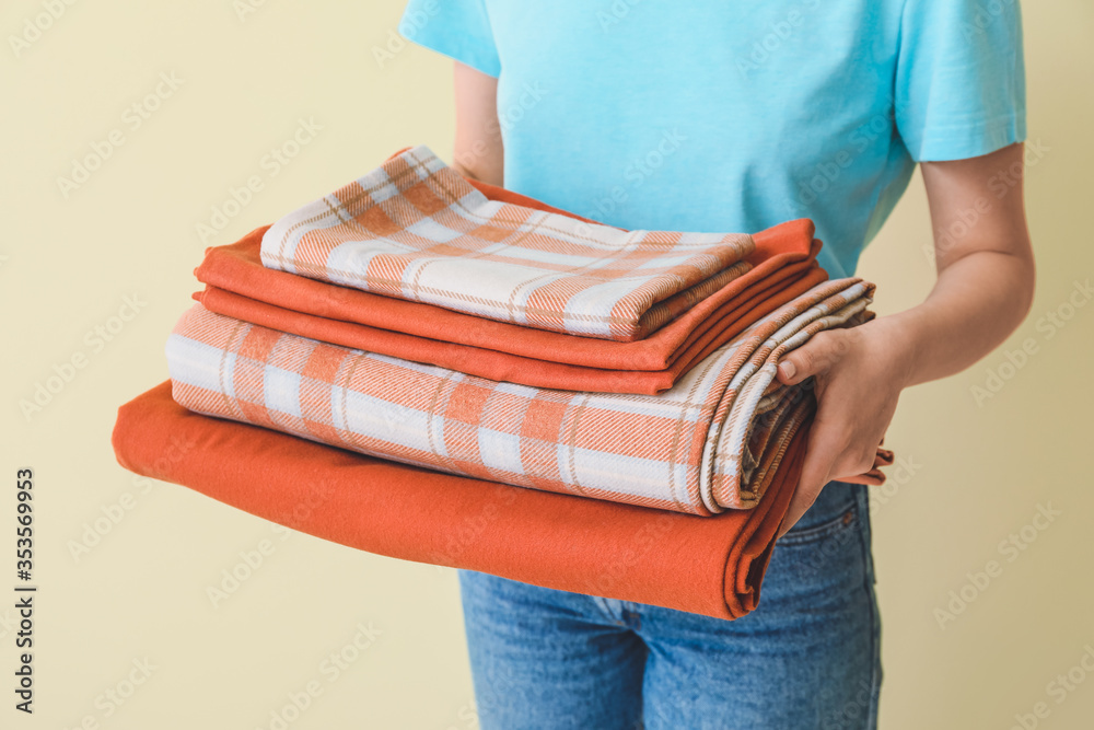 Woman holding stack of clean bed sheets on color background