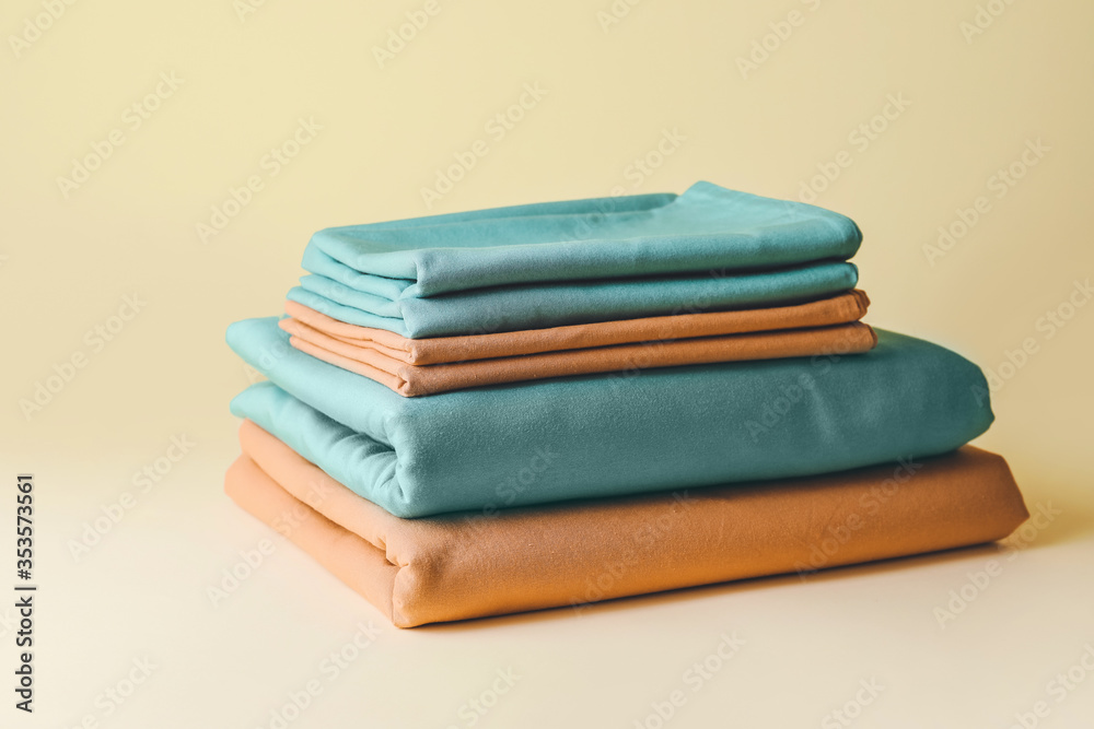 Stack of clean bed sheets on color background