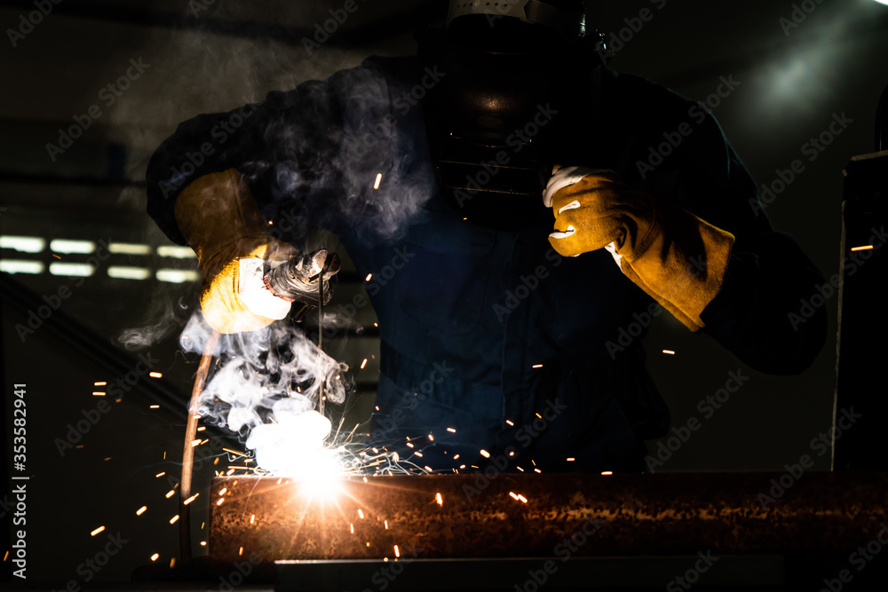 Metal welder working with arc welding machine to weld steel at factory while wearing safety equipmen