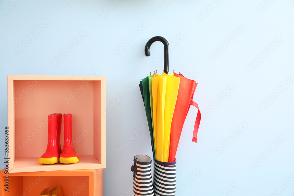 Stylish umbrella and gumboots near color wall