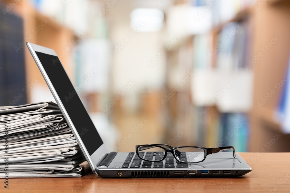 Laptop and newspapers stack on a table with a background