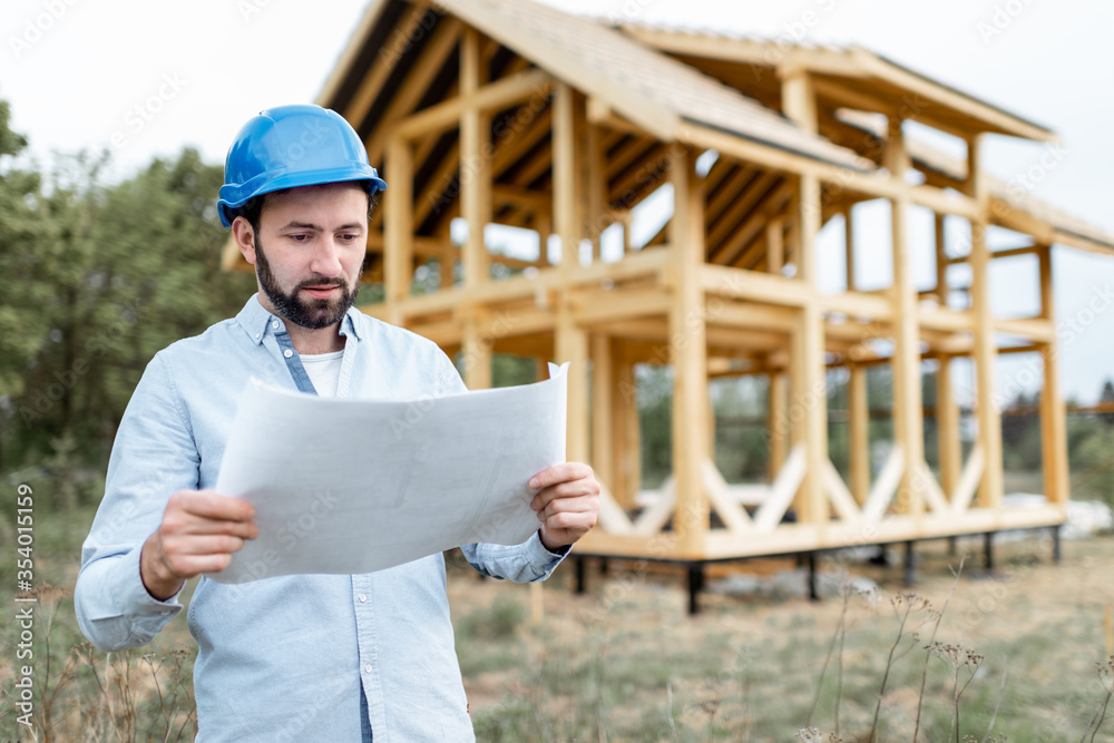 建筑师或建筑商拿着蓝图站在建筑工地上的木屋结构附近