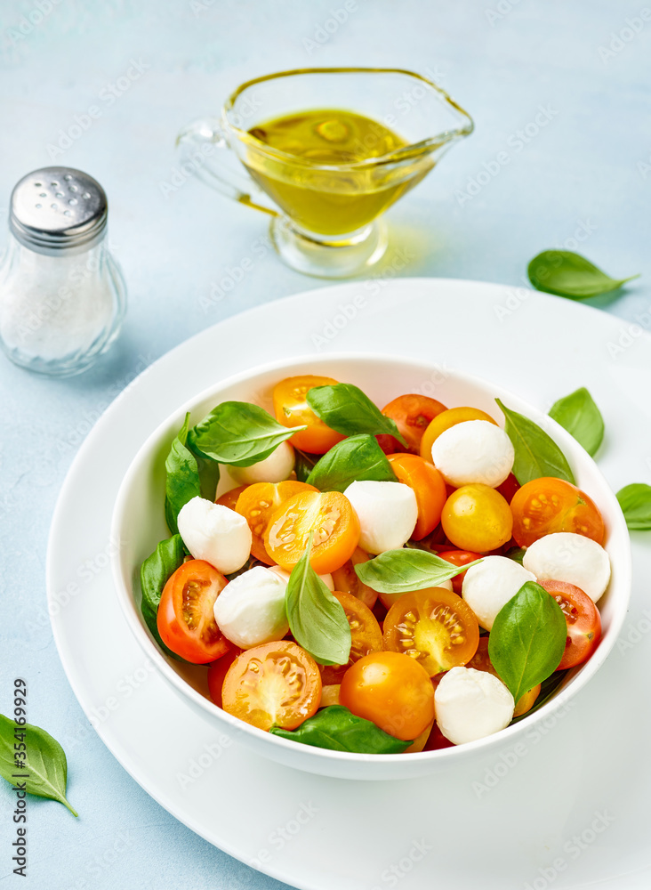 Caprese salad with yellow tomato cherry and mini mozzarella cheese in white bowl on white plate. Boc