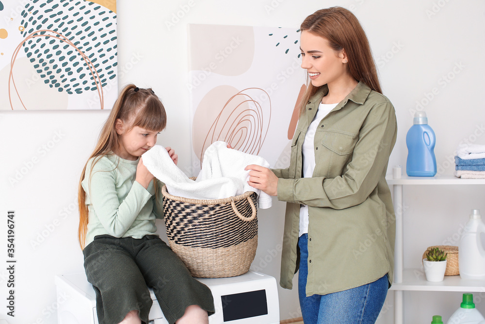 Woman and her cute little daughter doing laundry at home