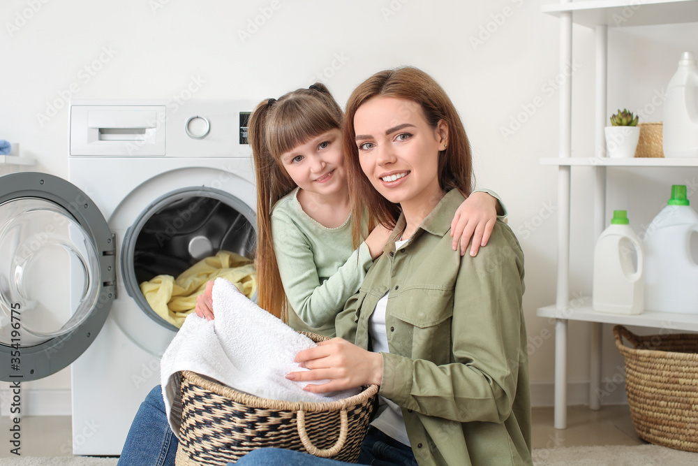 Woman and her cute little daughter doing laundry at home