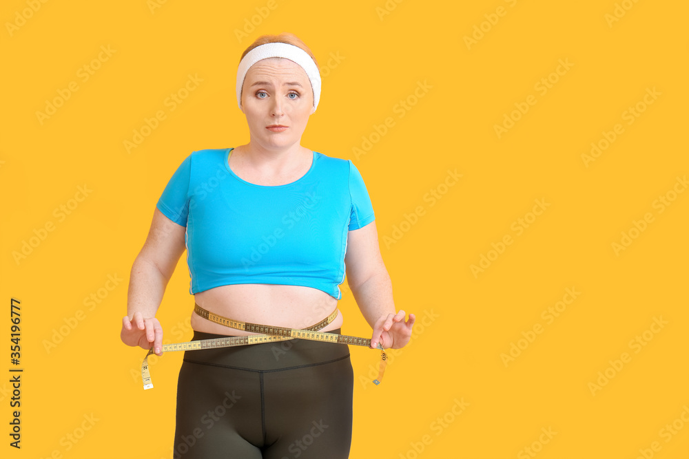 Woman with excess weight measuring her waist on color background