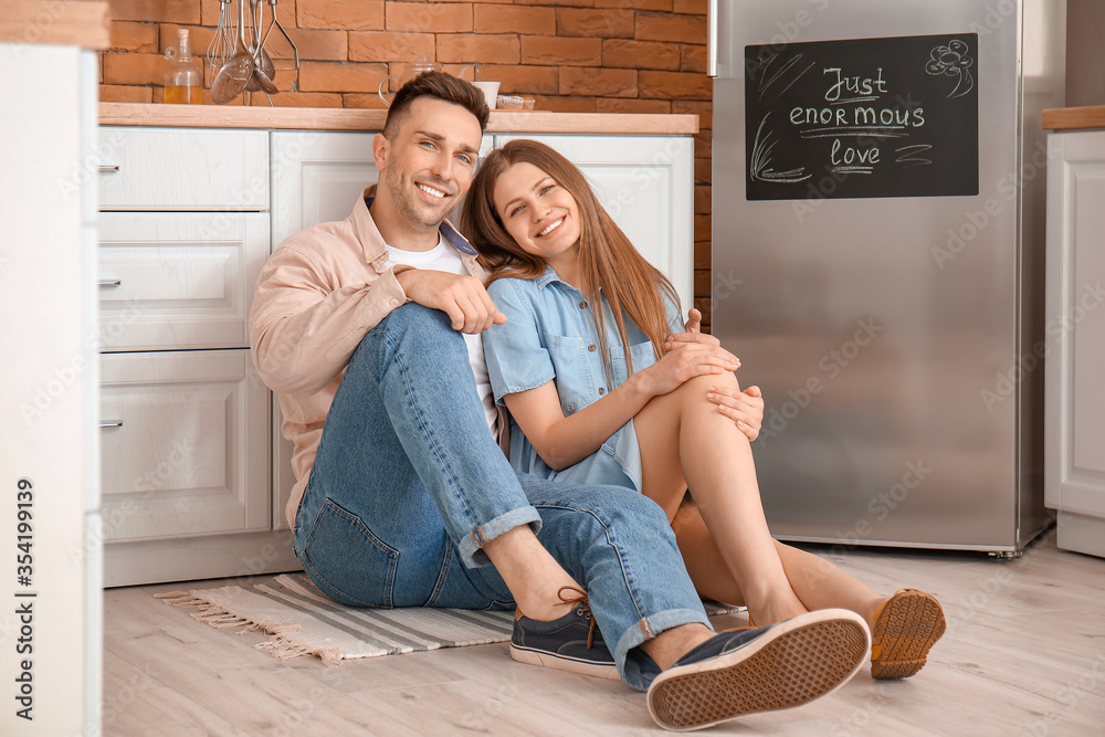 Happy couple sitting on floor near refrigerator in kitchen