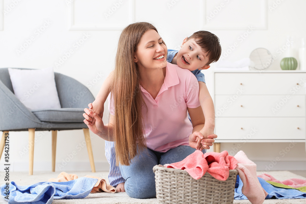 Young woman and her little son with clean laundry at home