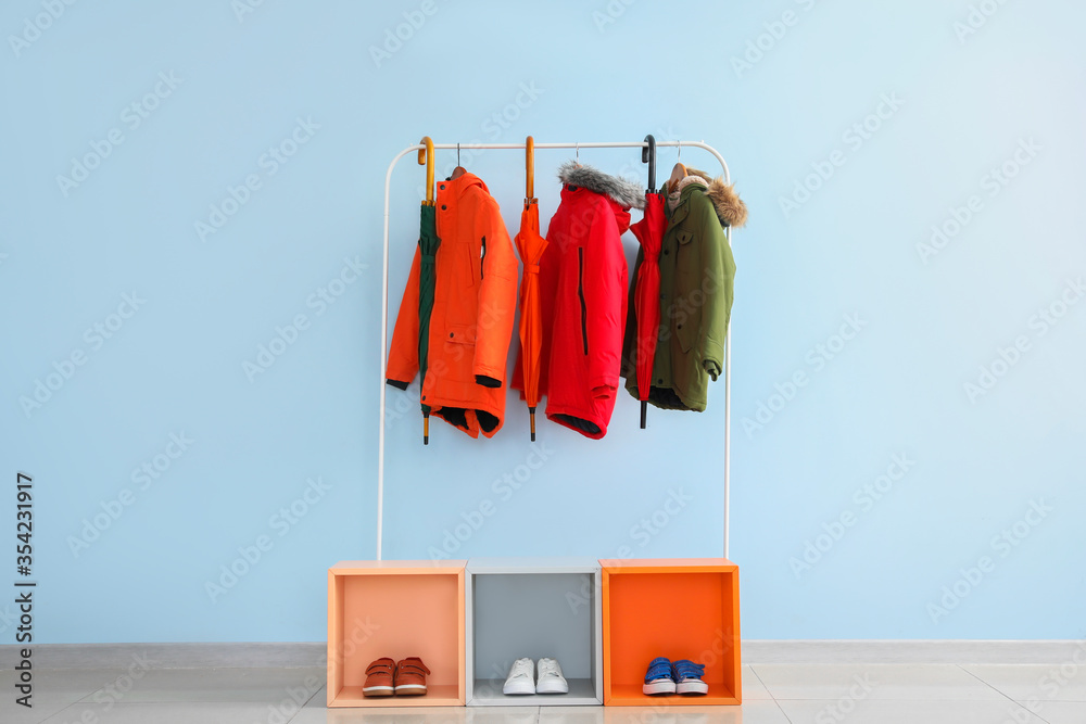 Stylish umbrellas, clothes and shoes near color wall