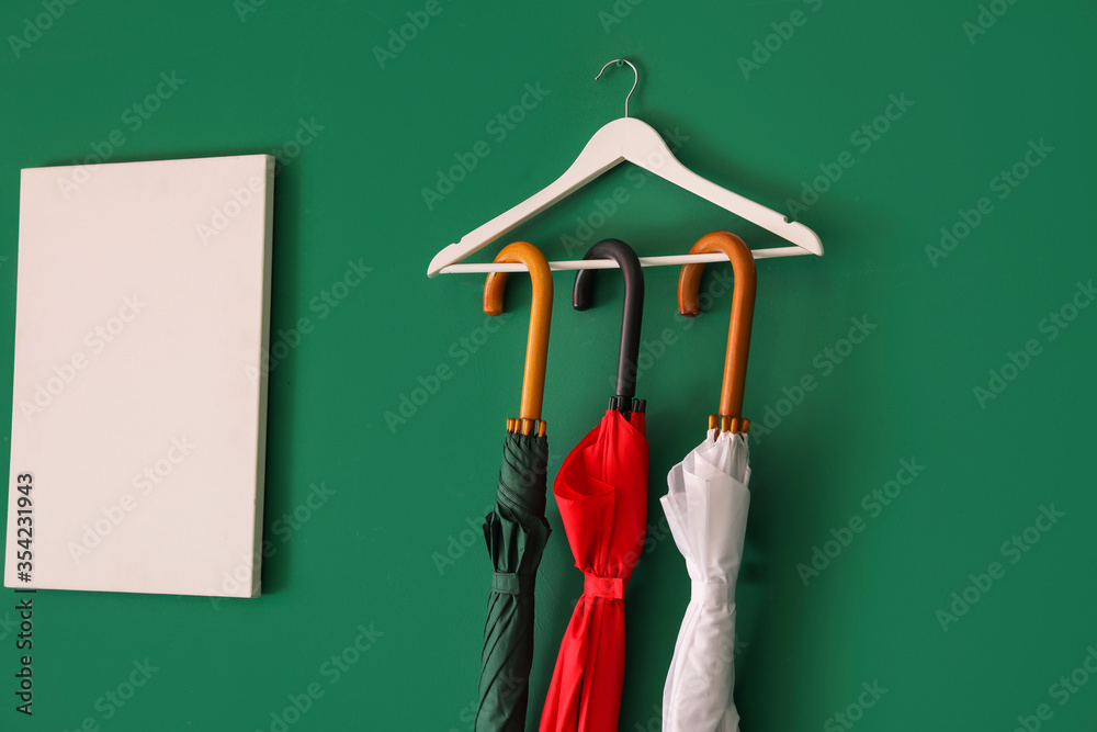 Stylish umbrellas hanging on color wall in hall