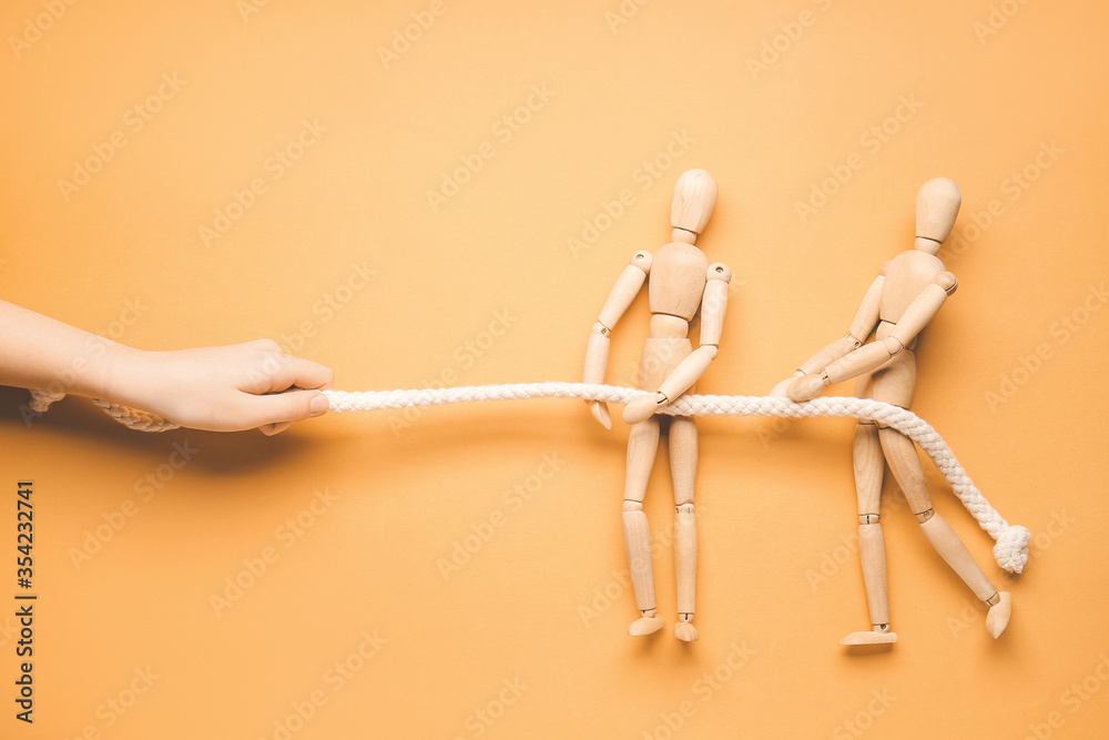 Female hand and wooden human figures pulling rope on color background. Unity concept