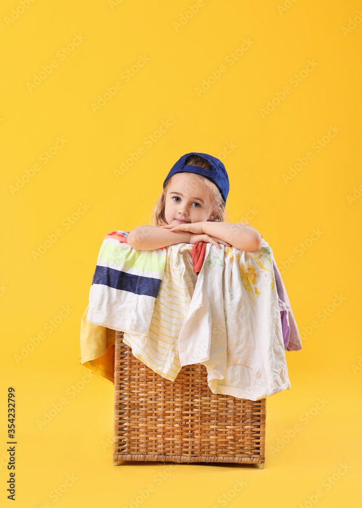 Cute little girl in basket with dirty laundry on color background