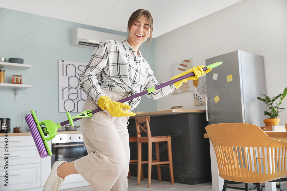 Young woman having fun while cleaning kitchen