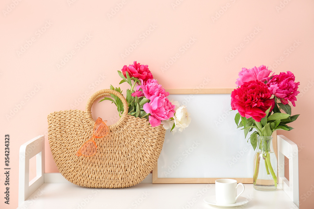 Beautiful peony flowers with bag and cup of coffee on table in room