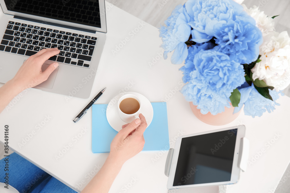 Woman working at table with beautiful peony flowers, top view